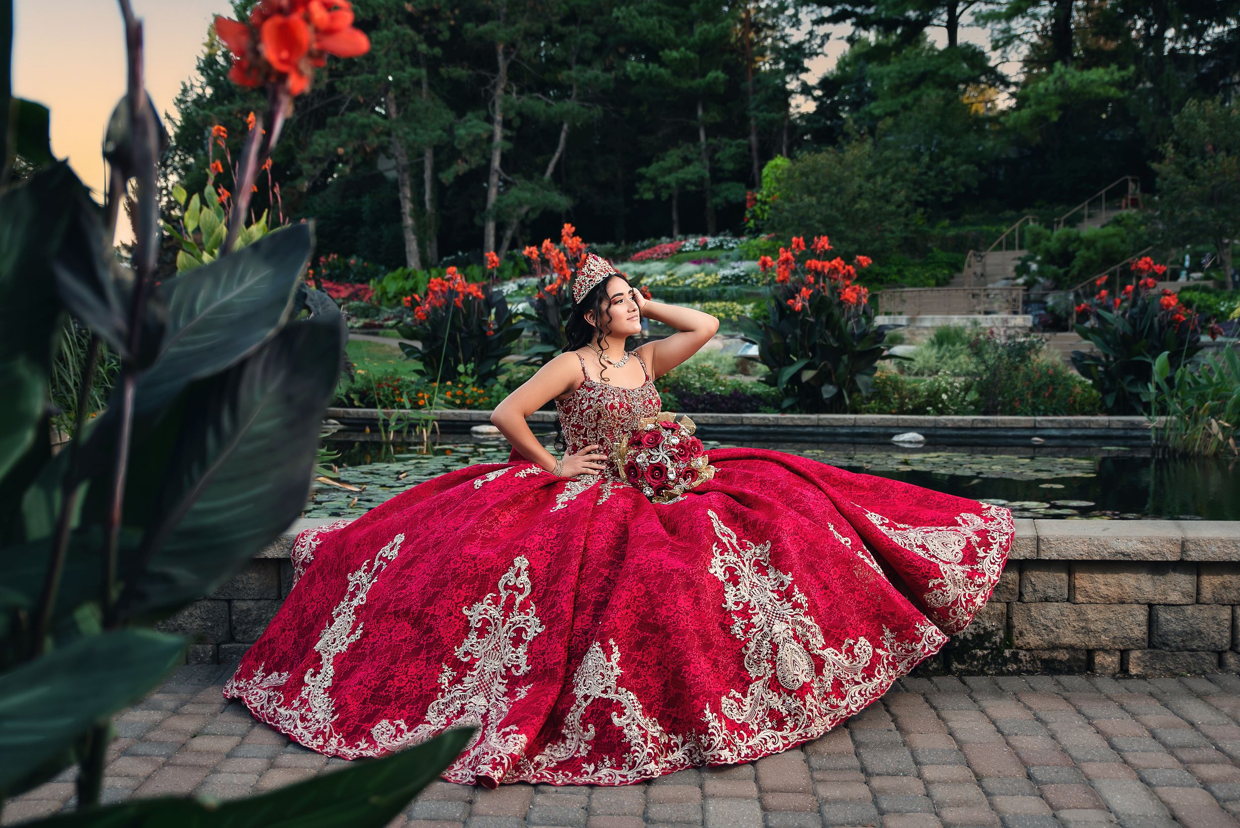 Stunning red formal dress with intricate gold details captured in a scenic garden location.