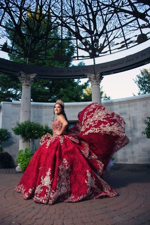 A red embellished ballgown photographed under a curved architectural structure with columns.