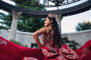 A dramatic red formal dress captured under an outdoor pavilion with classical architecture.