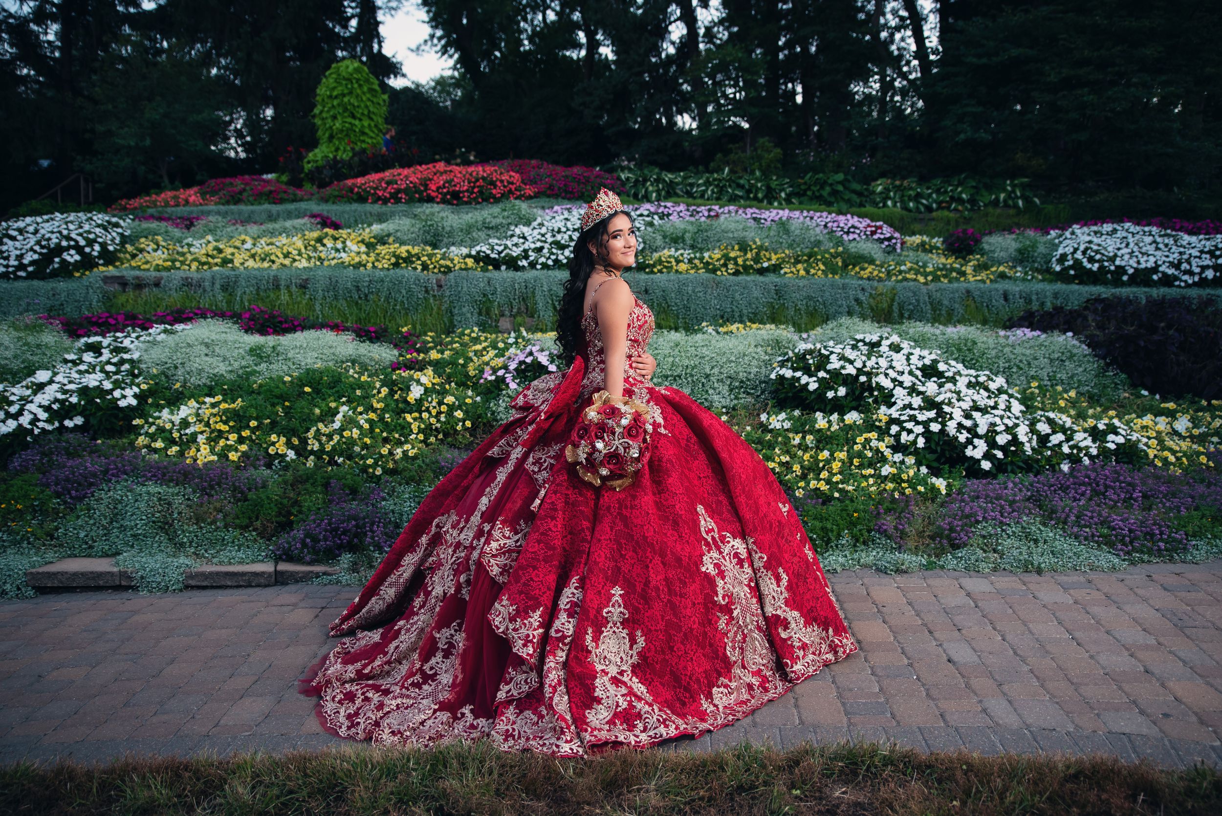 A dramatic red ballgown photographed in a garden setting with colorful flowers.