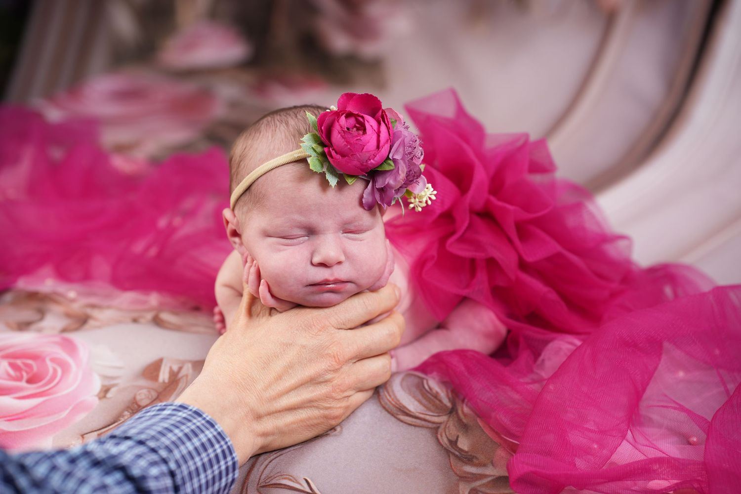A sleeping baby in pink tulle tutu and floral headband poses on soft pink fabric with rose petals.