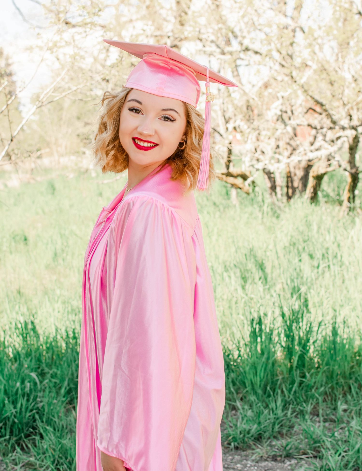 Spring fashion shoot in pink attire against blooming trees and green grass backdrop.