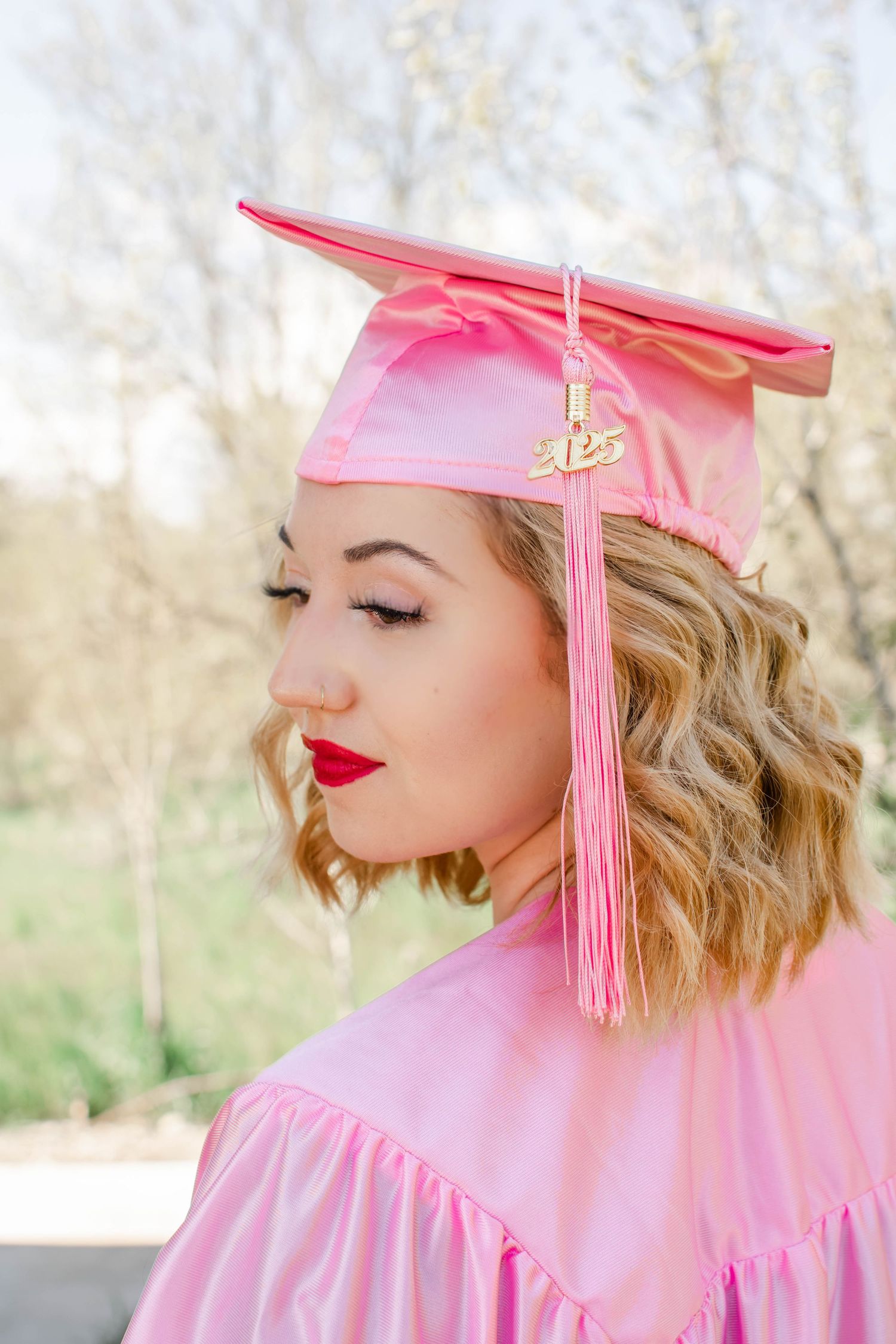 Pink graduation cap with tassel against spring background.