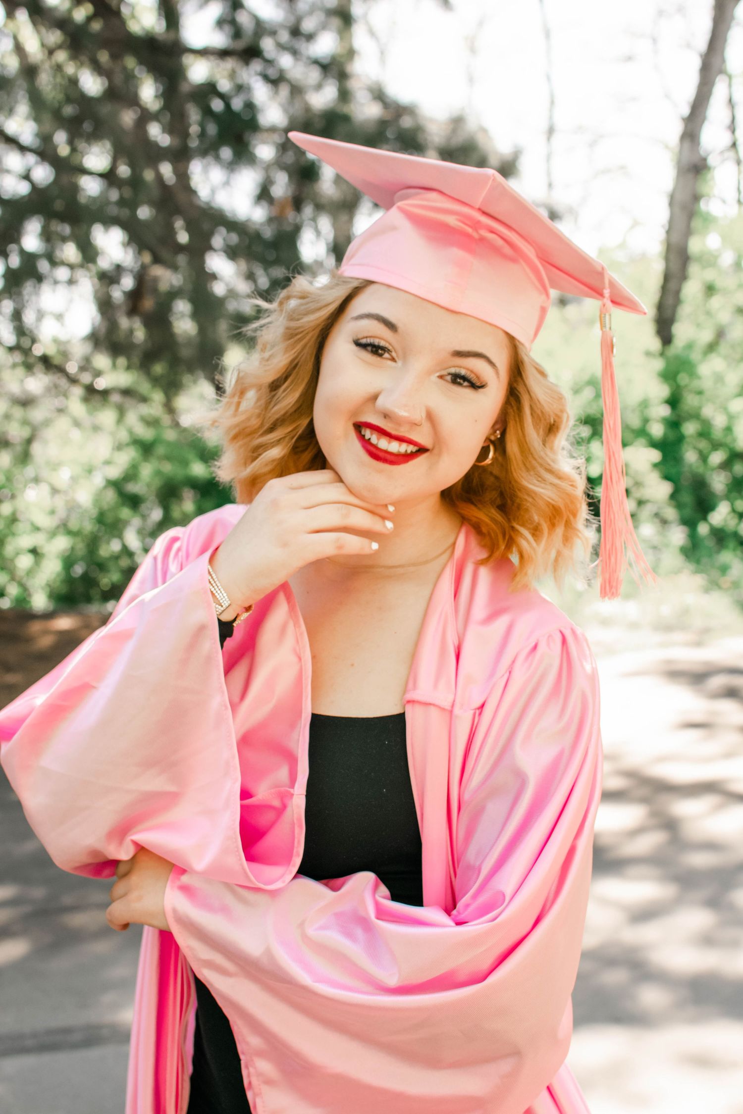 Joyful graduation portraits in pink cap and gown against natural backdrop.