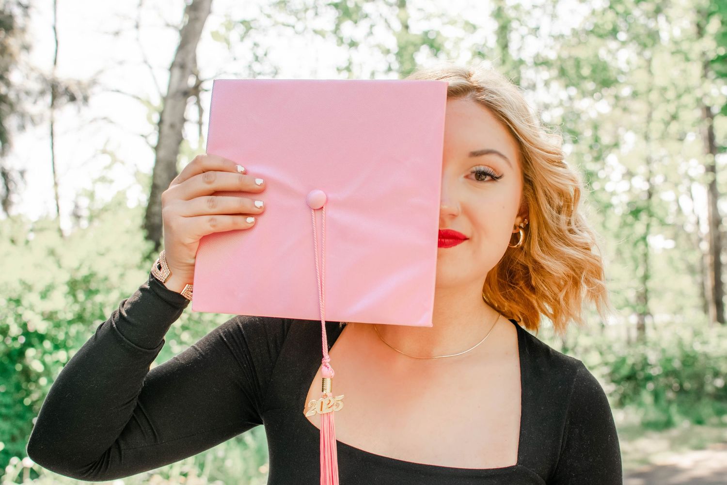Graduate holding up pink diploma cover during outdoor photoshoot.