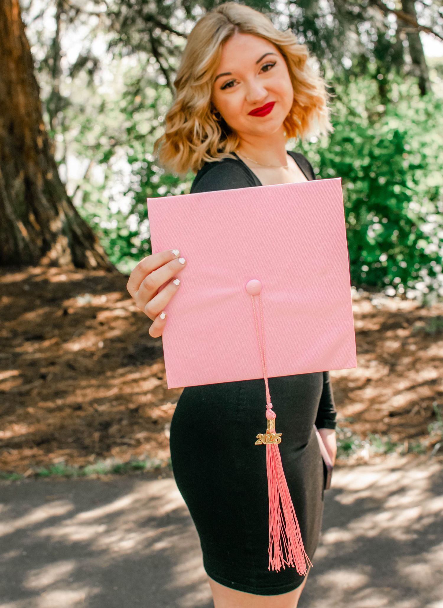 Outdoor graduation photos with student holding pink diploma cover in wooded setting.