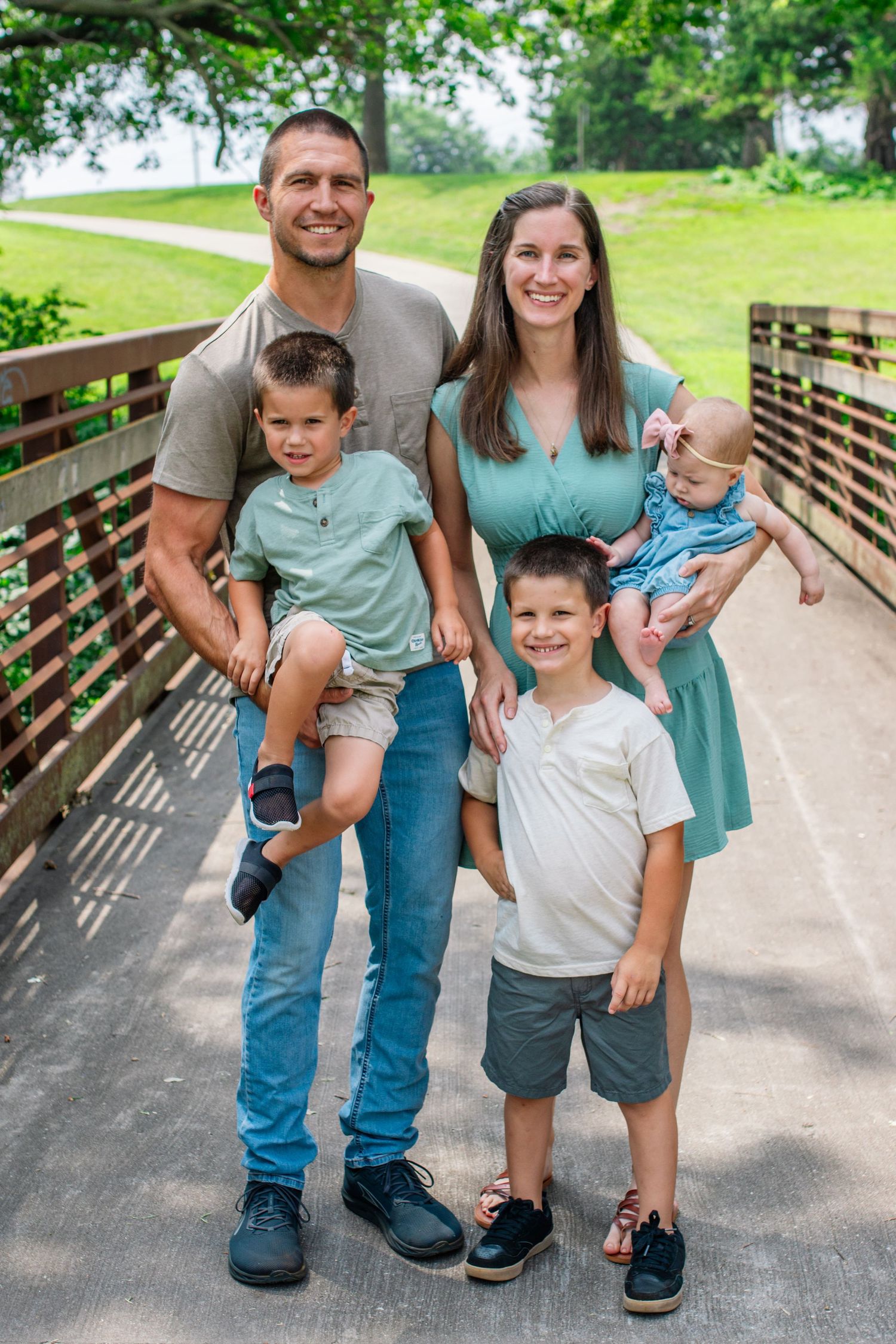 Family group standing together on a wooden bridge pathway in coordinated blue and teal outfits.