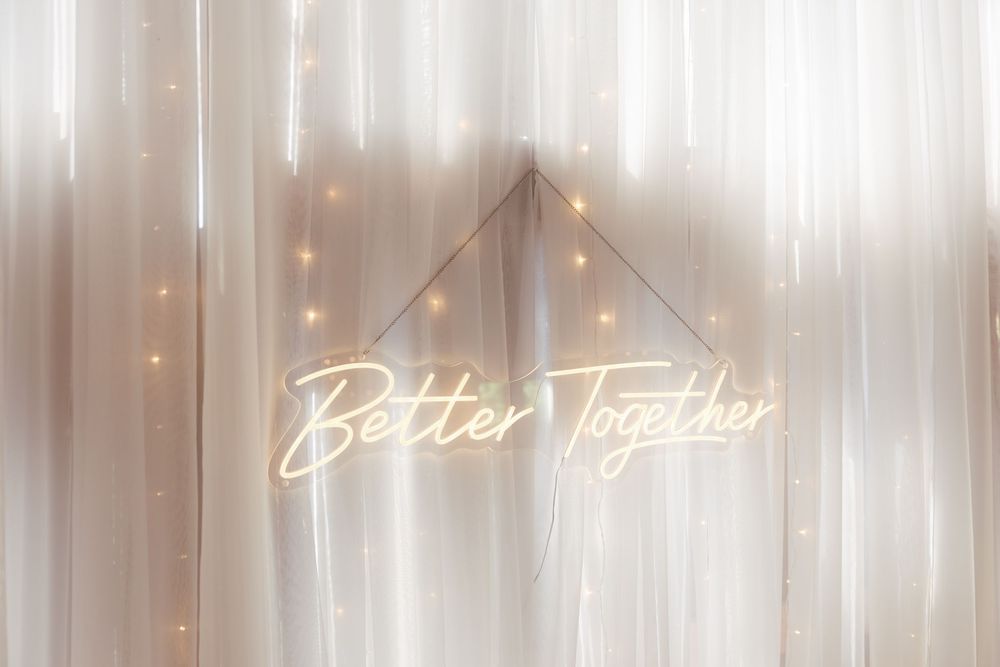 A rustic wooden wall with warm glowing string lights and illuminated 'Better Together' neon sign creating an intimate ambiance.