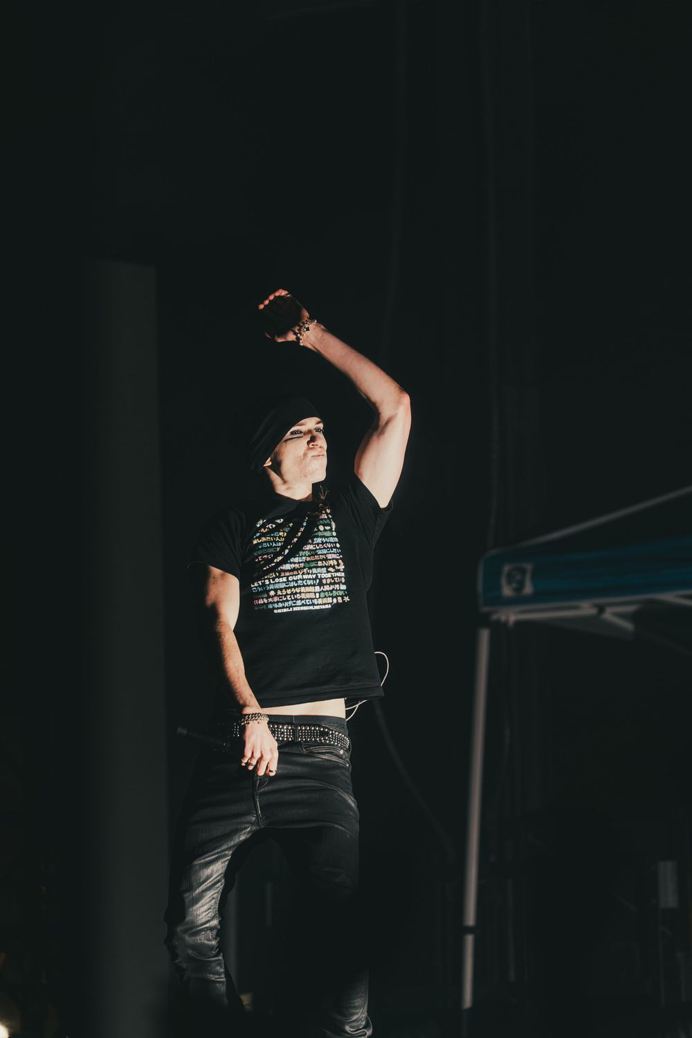 A performer in a black t-shirt and dark pants gestures dramatically on a dimly lit stage during a show.