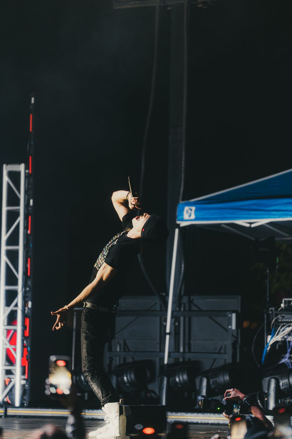 A performer in dark clothing leaps energetically on stage during an outdoor concert performance.