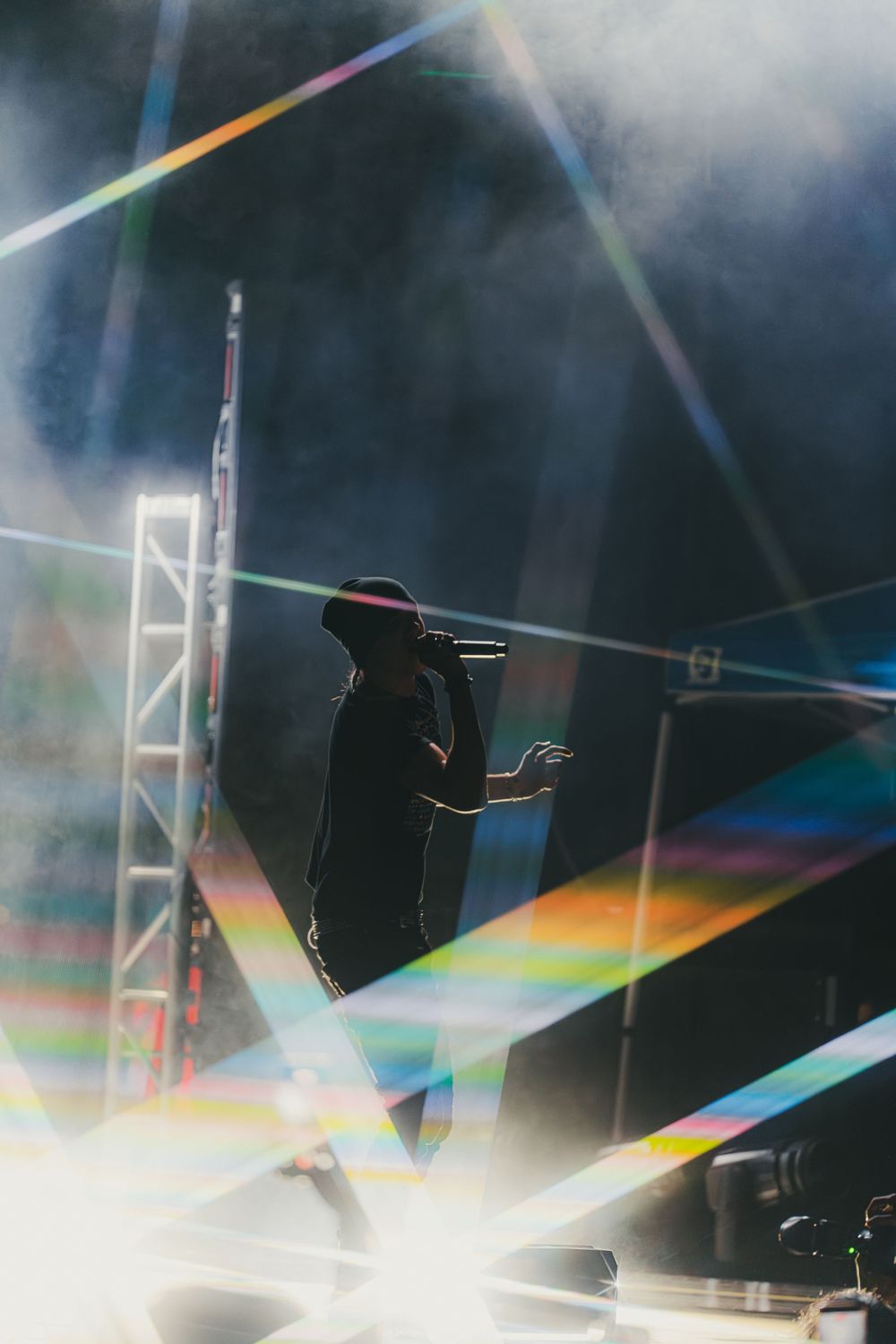 Abstract light reflections create a prismatic rainbow effect against a dark background with silhouetted shapes.