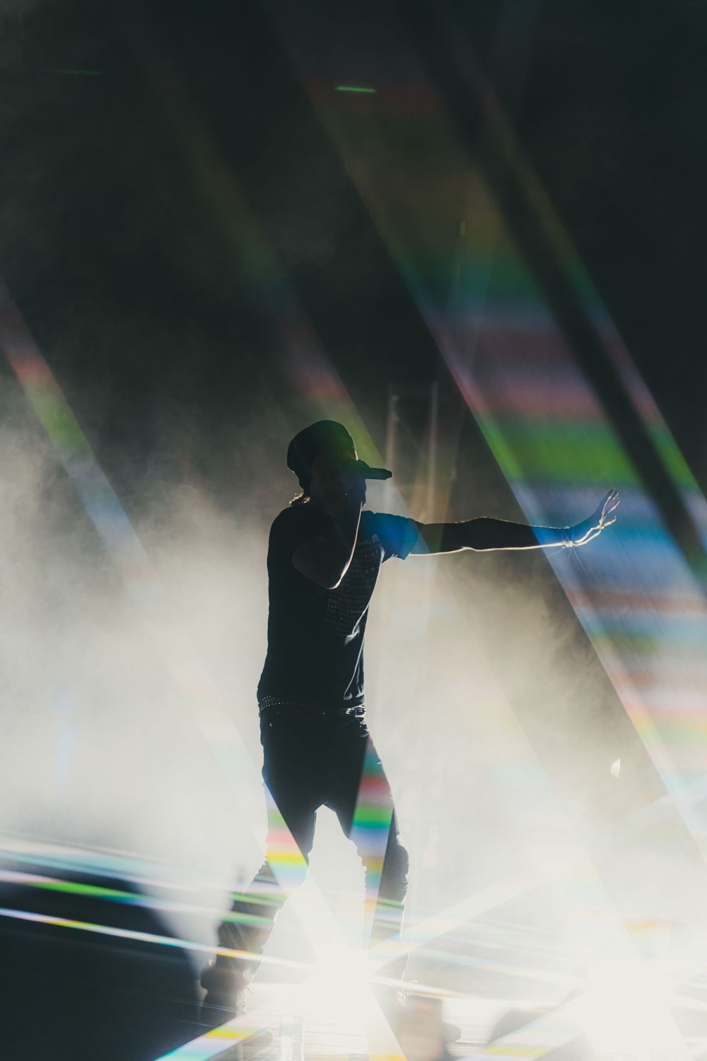 Silhouette of a performer with outstretched arms amid atmospheric stage fog and colorful light beams.