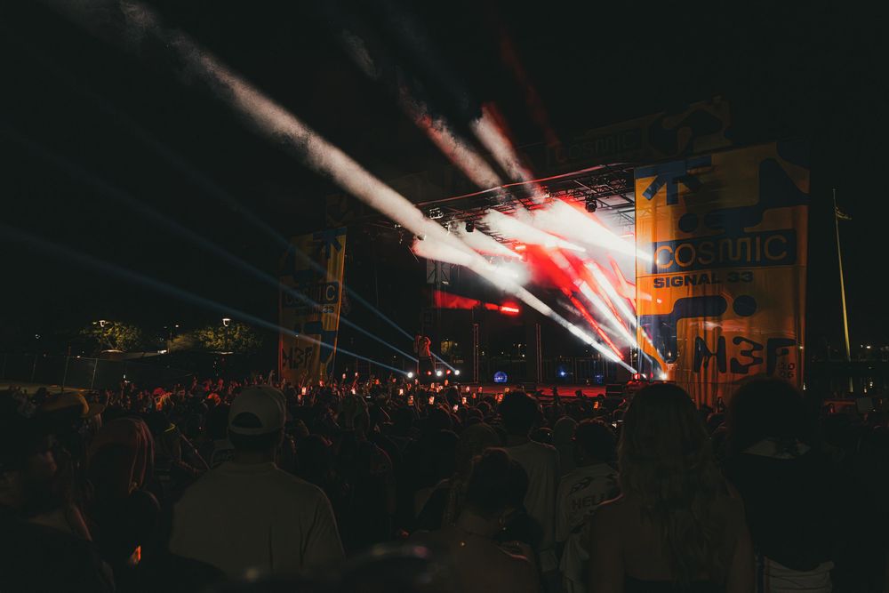 A large crowd watches a vibrant red and white light display at an outdoor concert or festival at night.