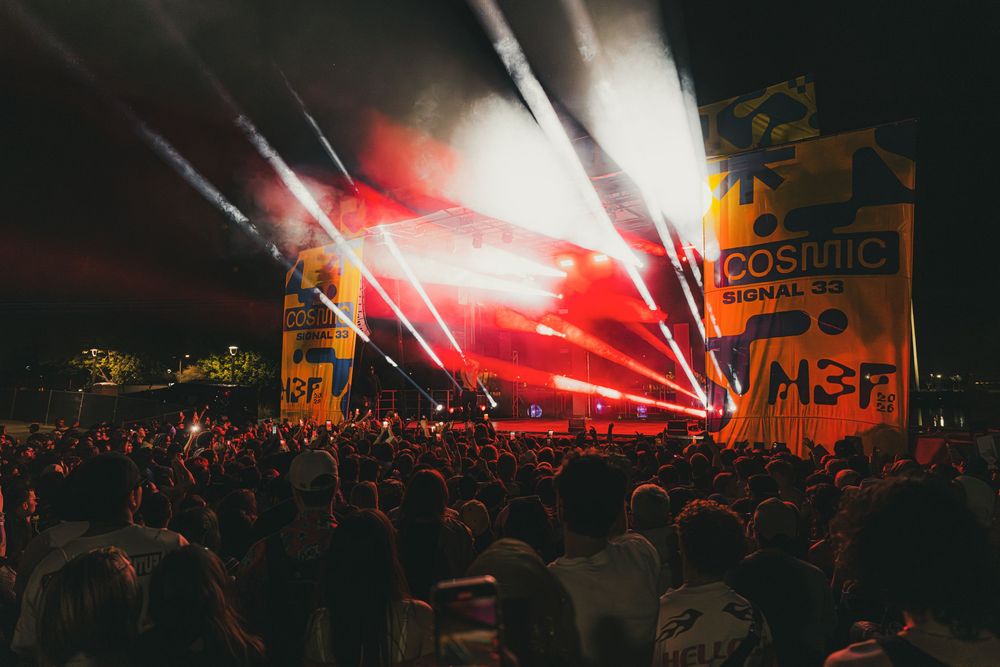 Red flares illuminate a crowded nighttime gathering as fans wave flags and banners at a sporting event.