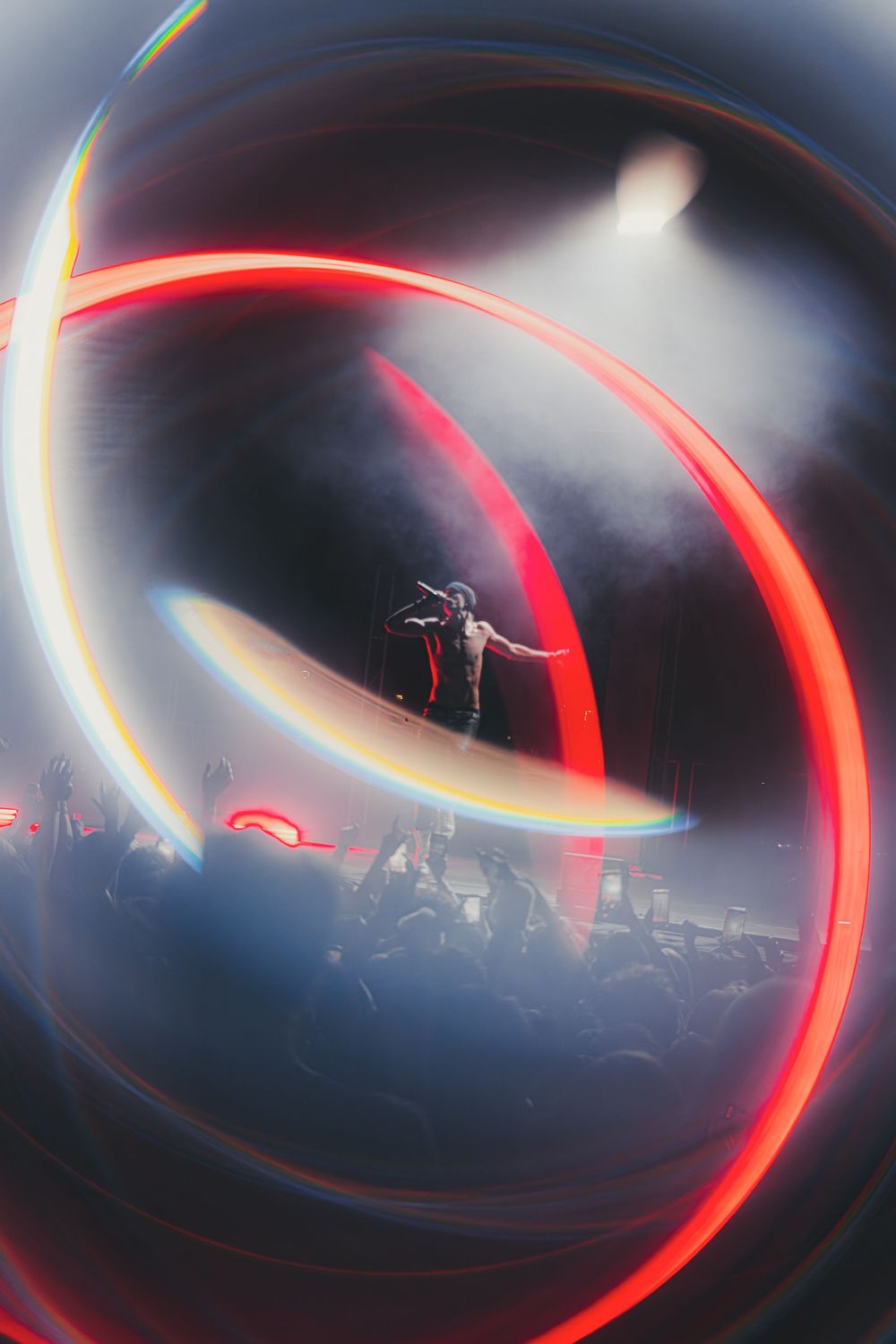 Concert performer on stage surrounded by dramatic red light trails and swirling effects creating a dynamic atmosphere.
