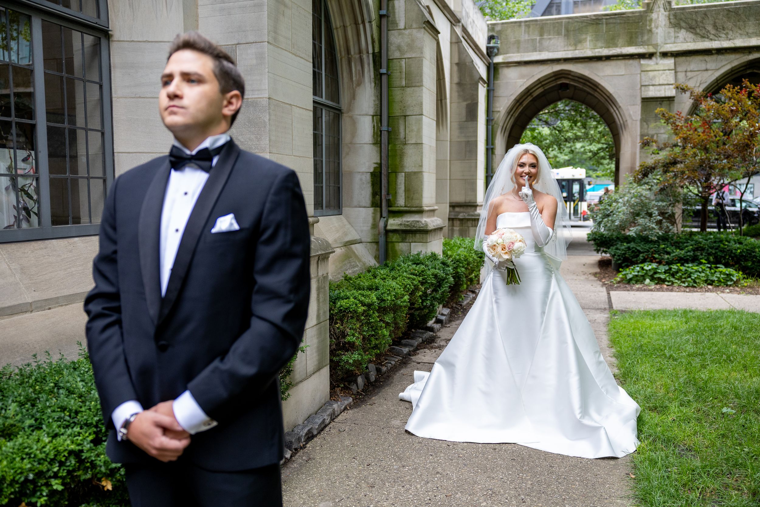 A wedding couple poses in an elegant stone courtyard with Gothic architectural details and greenery.