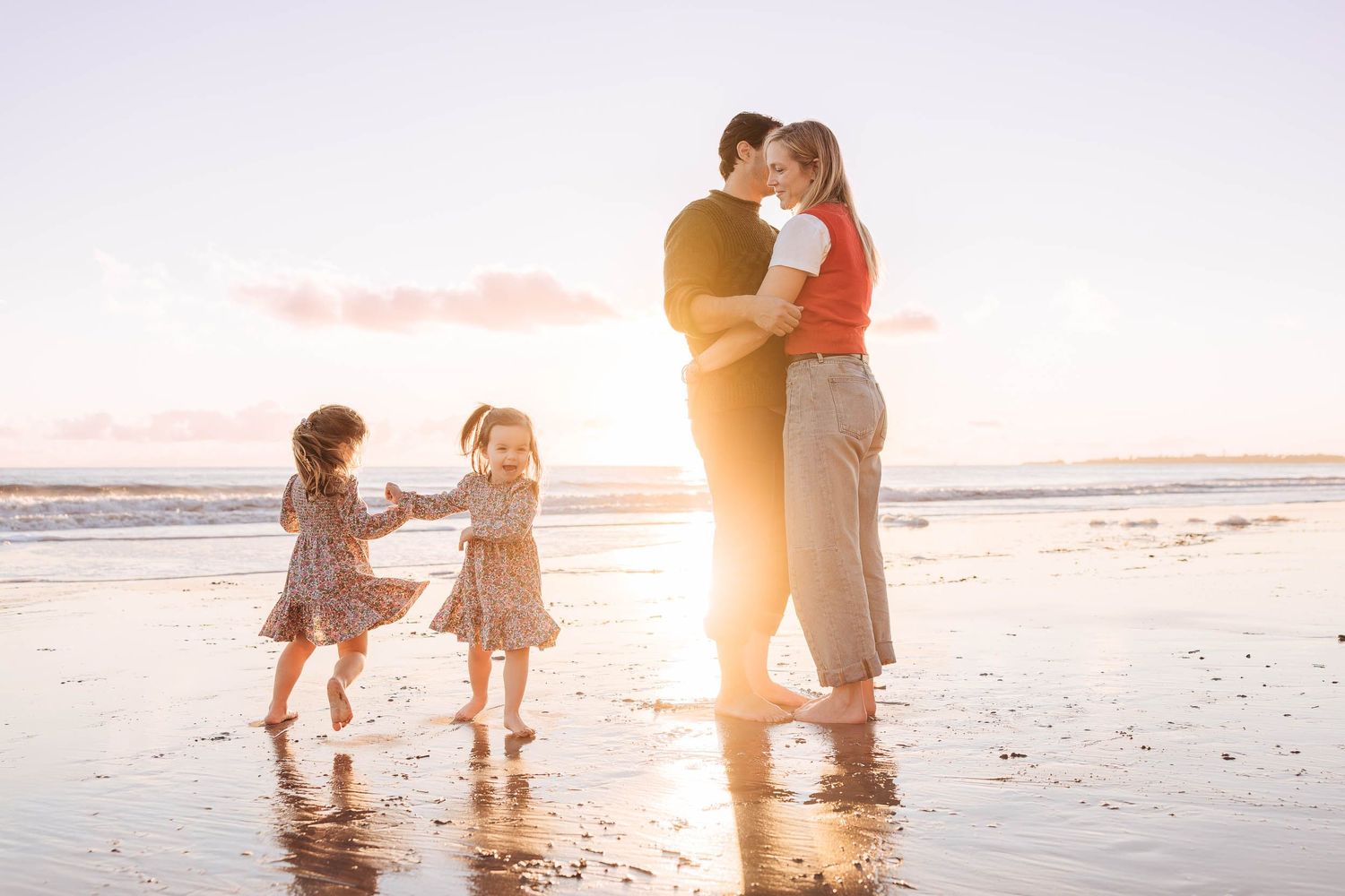 Family playing together on sandy beach at sunset with waves and golden light in background.