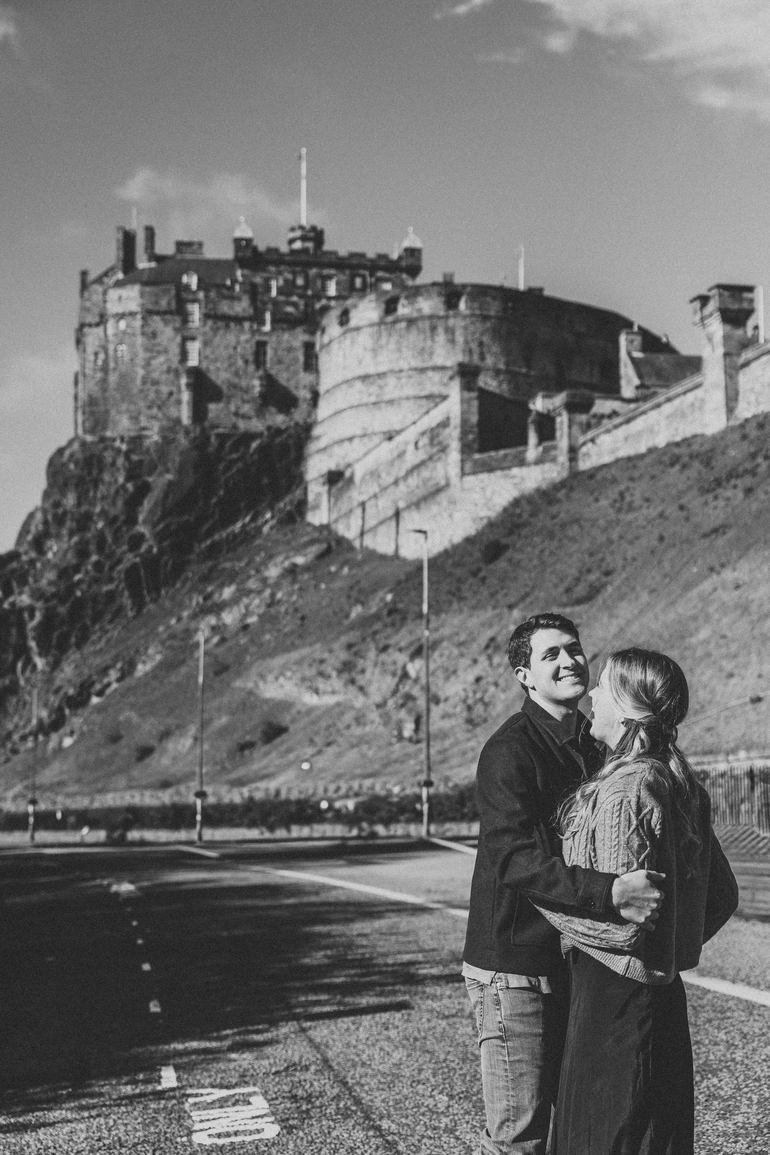 A romantic couple shares intimate moments against the backdrop of Edinburgh Castle on a cloudy day.