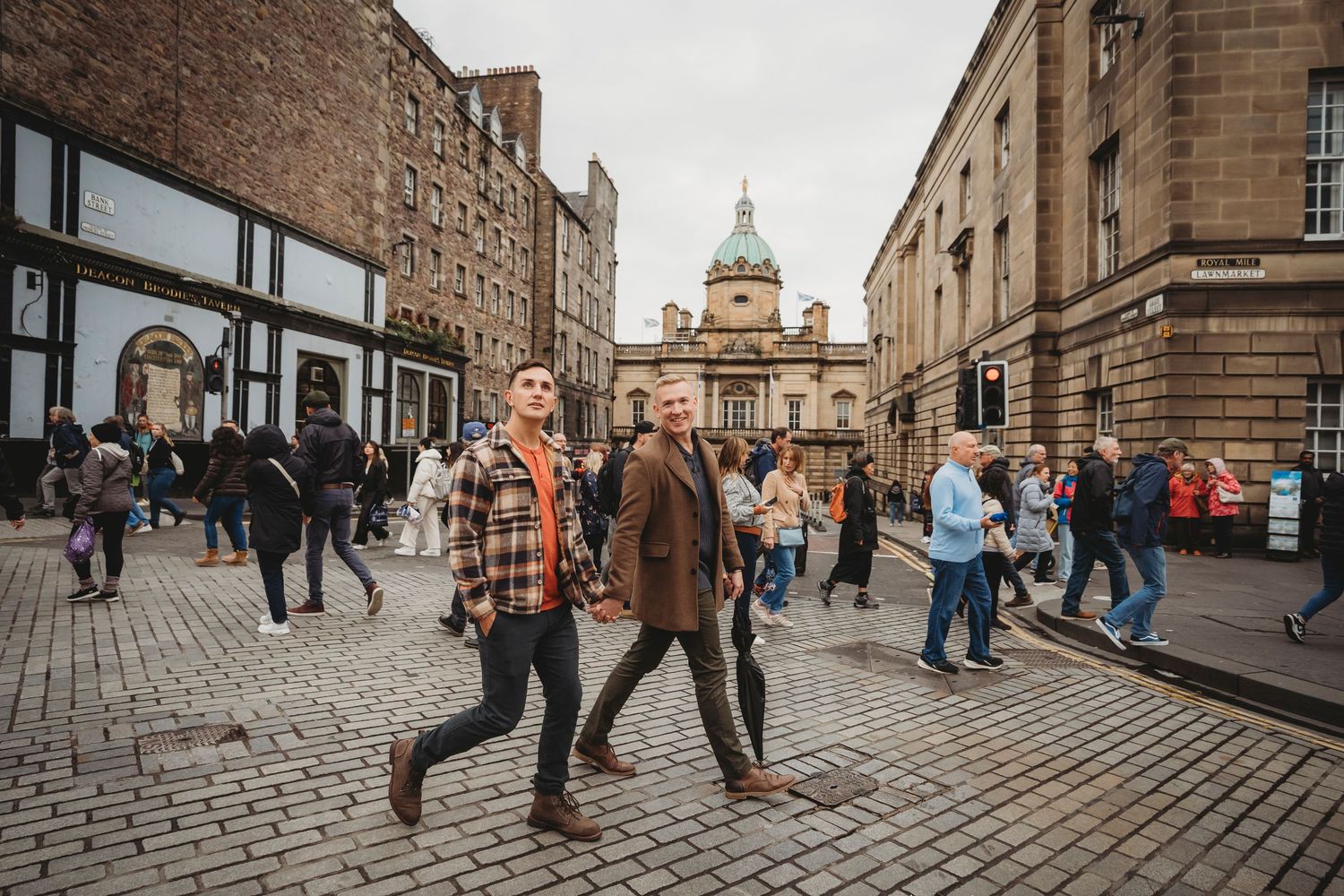 Wide angle panoramic view of a historic cobblestone street in Edinburgh with stone buildings and pedestrians walking.