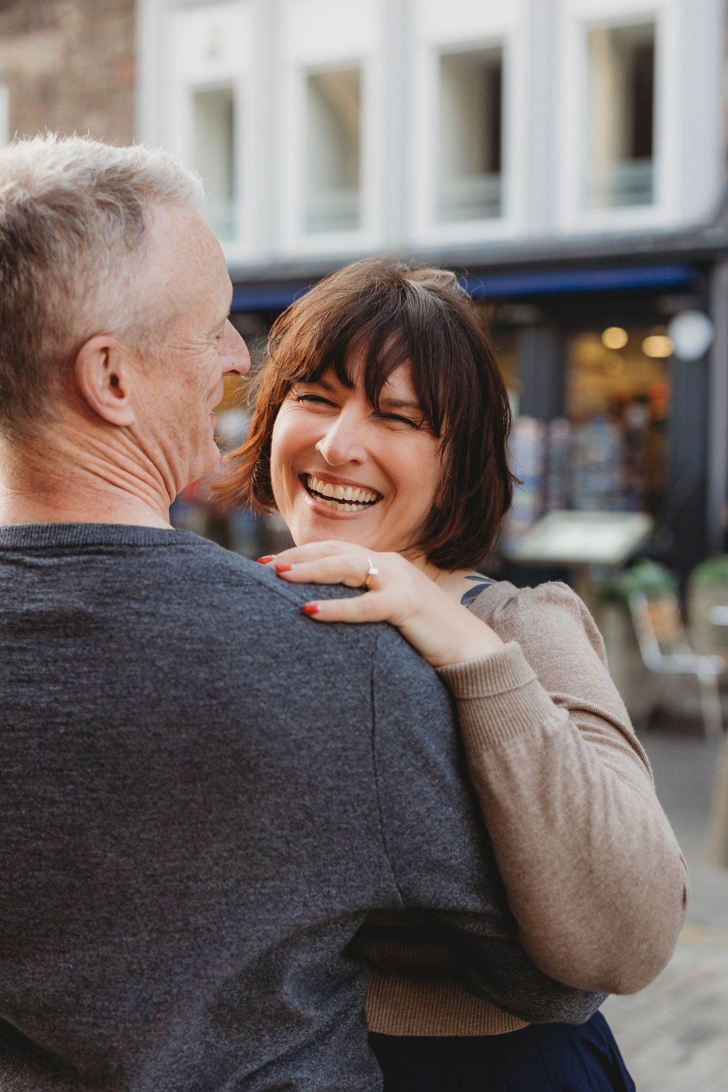 Two people share a joyful moment together on a city street, one wearing a gray sweater and one in beige.