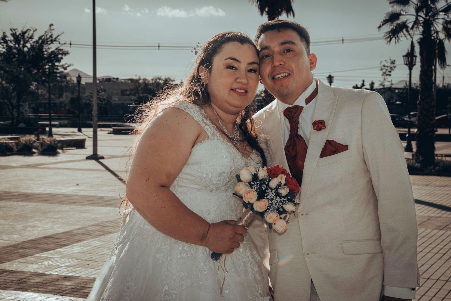 Retrato de boda al aire libre con palmeras y fondo iluminado por el sol.