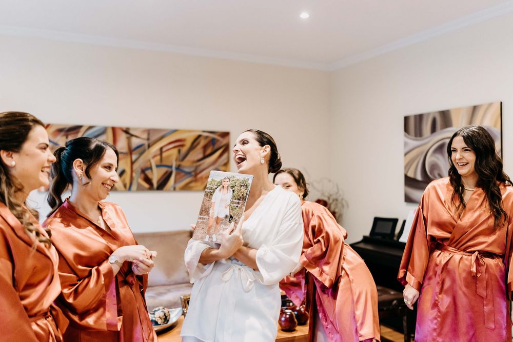 Bridesmaids in matching peach-colored robes share joyful moments while getting ready for a wedding celebration.