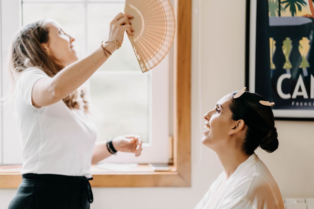 A couple in white outfits dance together during a wedding celebration in a sunlit room with framed artwork.