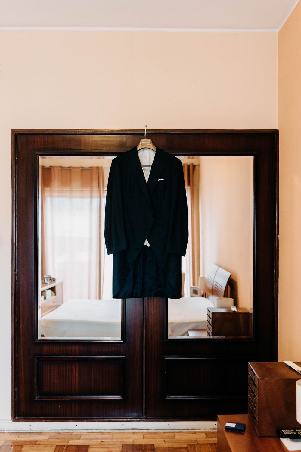 A black suit jacket hangs on display in a room with wooden frames and cream-colored walls.
