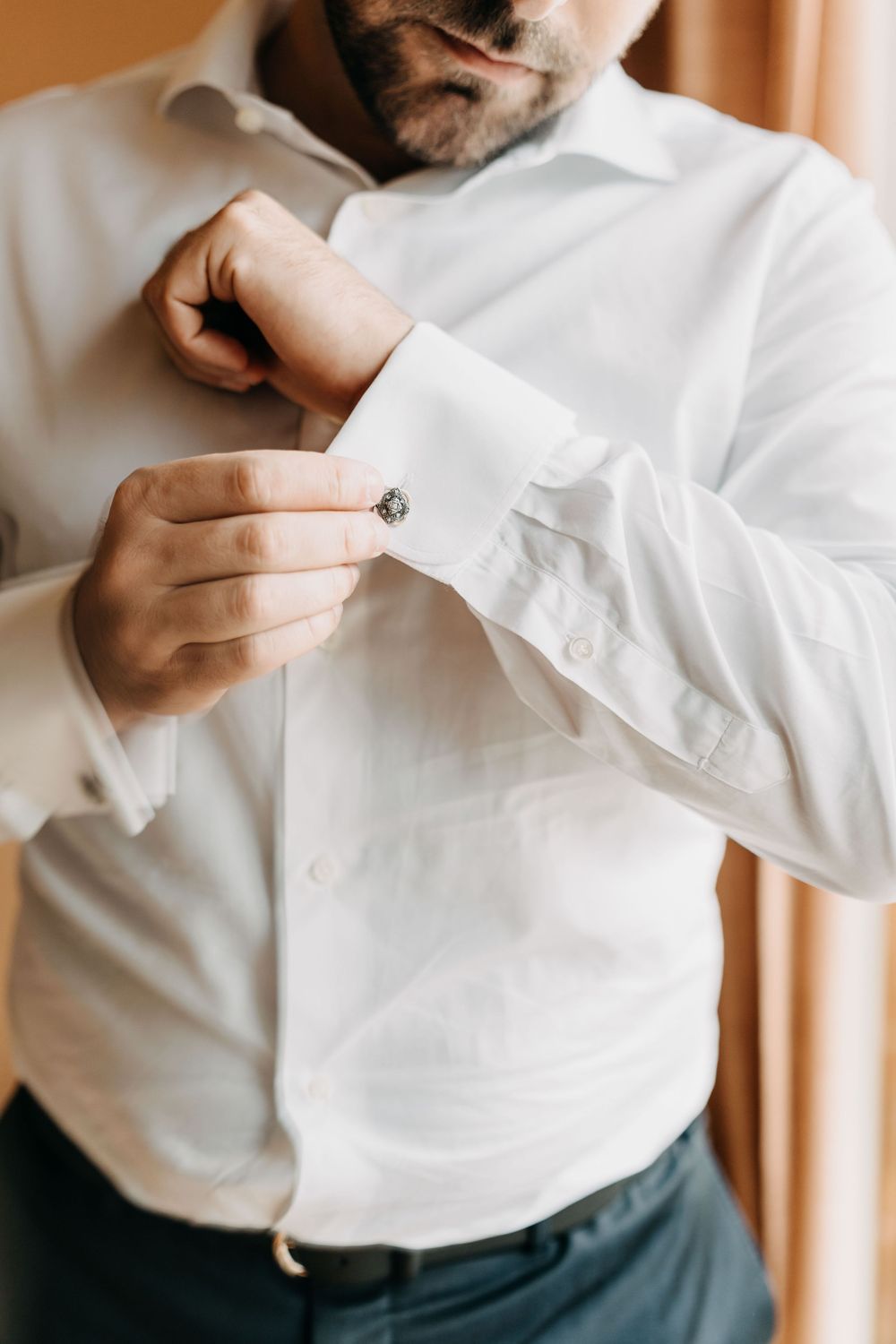 Close-up view of someone fastening buttons on a crisp white dress shirt sleeve.
