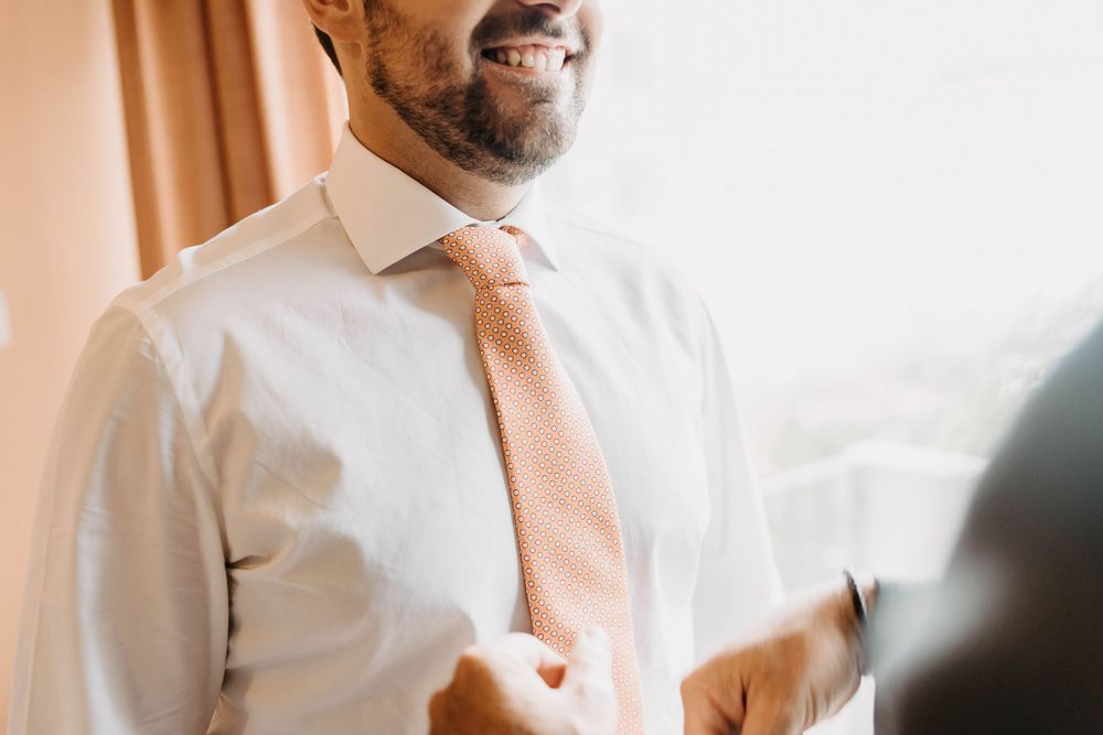 A person in a white button-down shirt smiles warmly while standing in a bright interior setting.