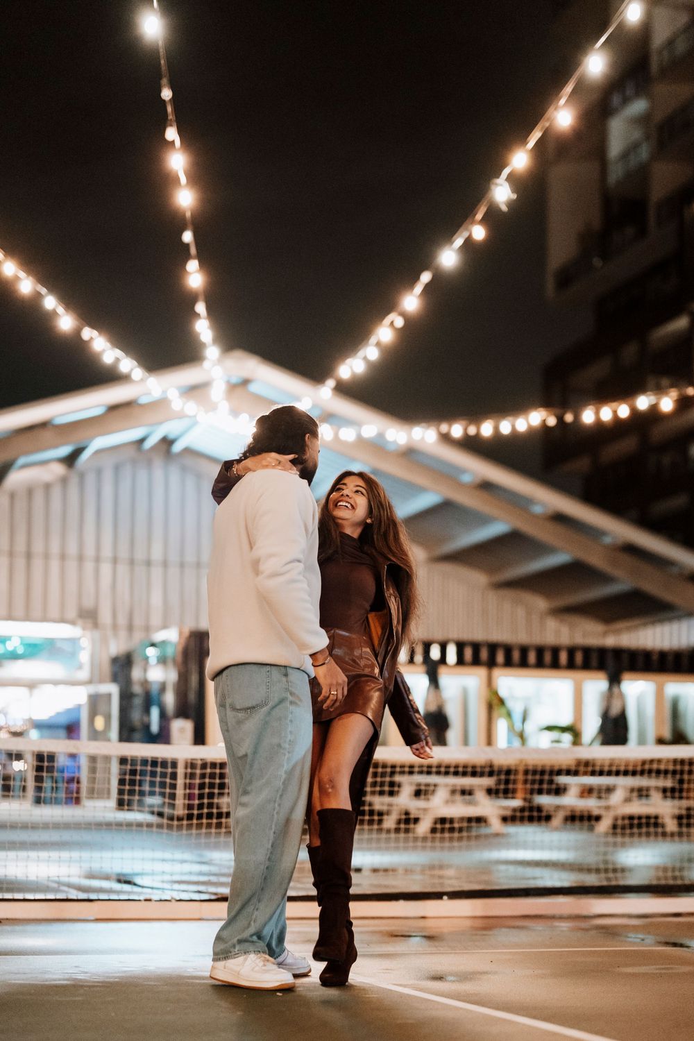 String lights illuminate an ice skating rink as skaters glide across the smooth surface at night.