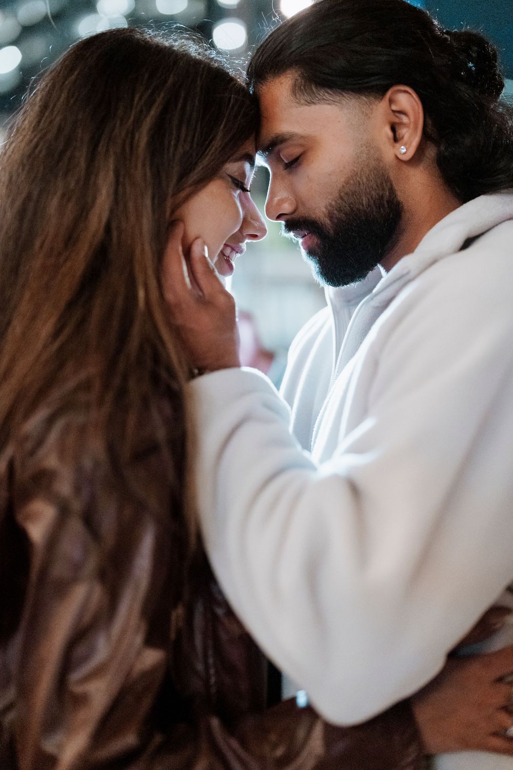 A romantic couple in white clothing share an intimate embrace against a soft bokeh background.