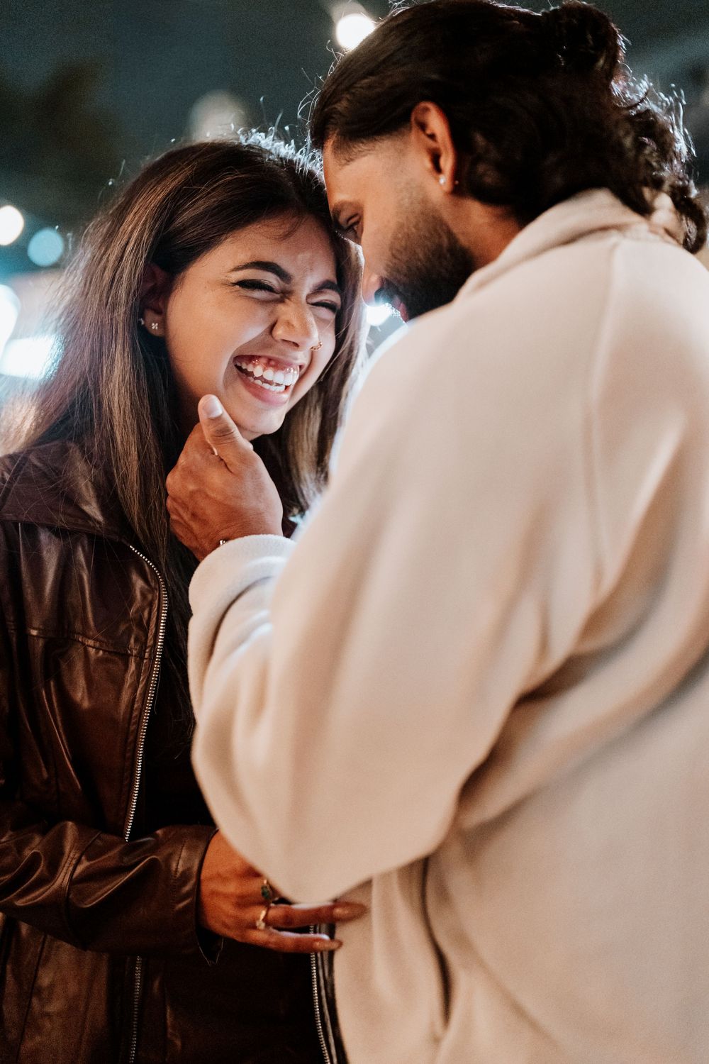 A couple shares a joyful embrace and laugh together while wearing contrasting dark and light colored outerwear.