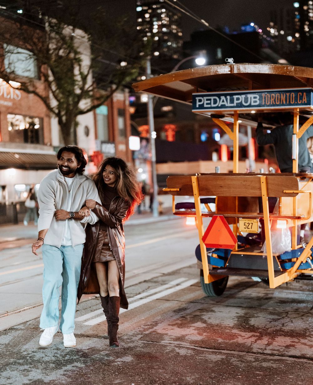 Night scene showing illuminated Pedal Pub sign and people walking on a city street.