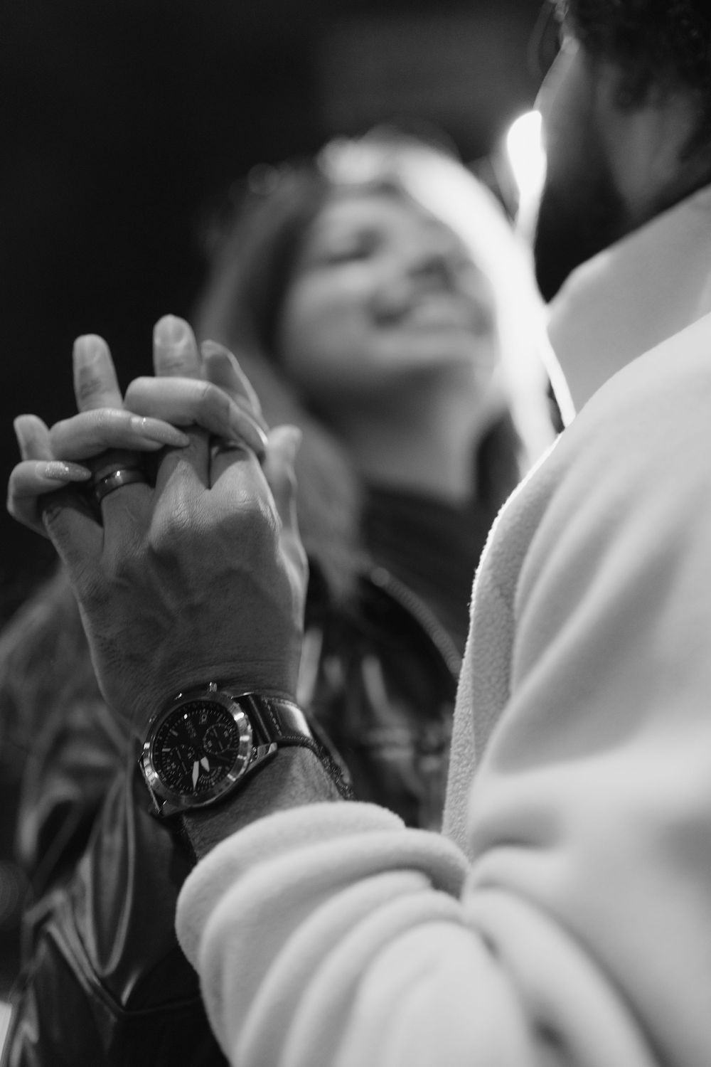 Close-up black and white photo showing clasped hands with a wristwatch visible in an intimate moment.