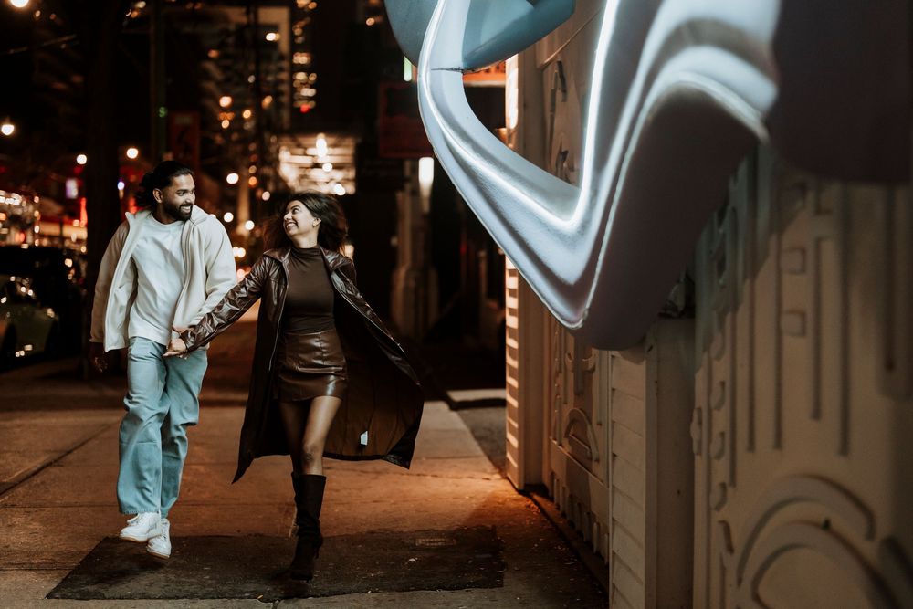Person in a light blue outfit walks past a graffiti-covered wall in an urban nighttime setting.