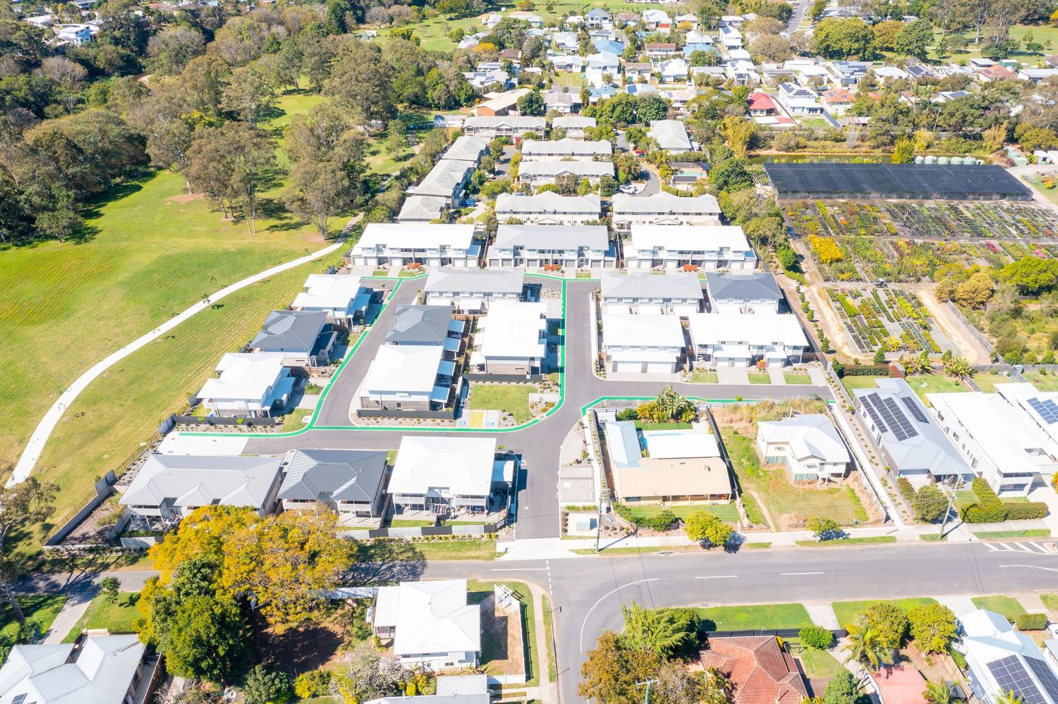 Aerial view of a modern residential development with multiple homes, green spaces, and solar panels in a suburban Queensland area.