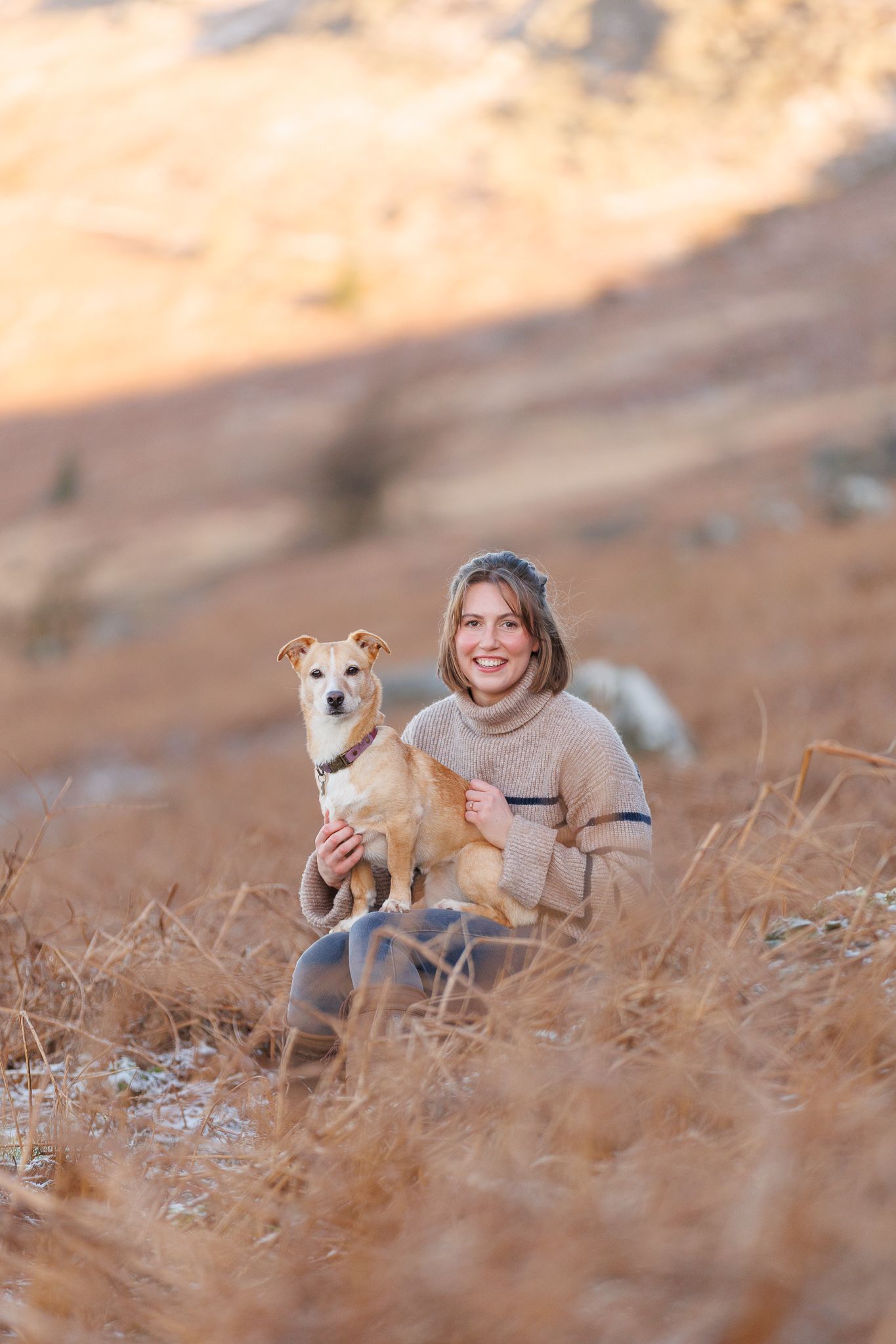 A person in a pink sweater and jeans stands with a black horse against a backdrop of golden autumn foliage.