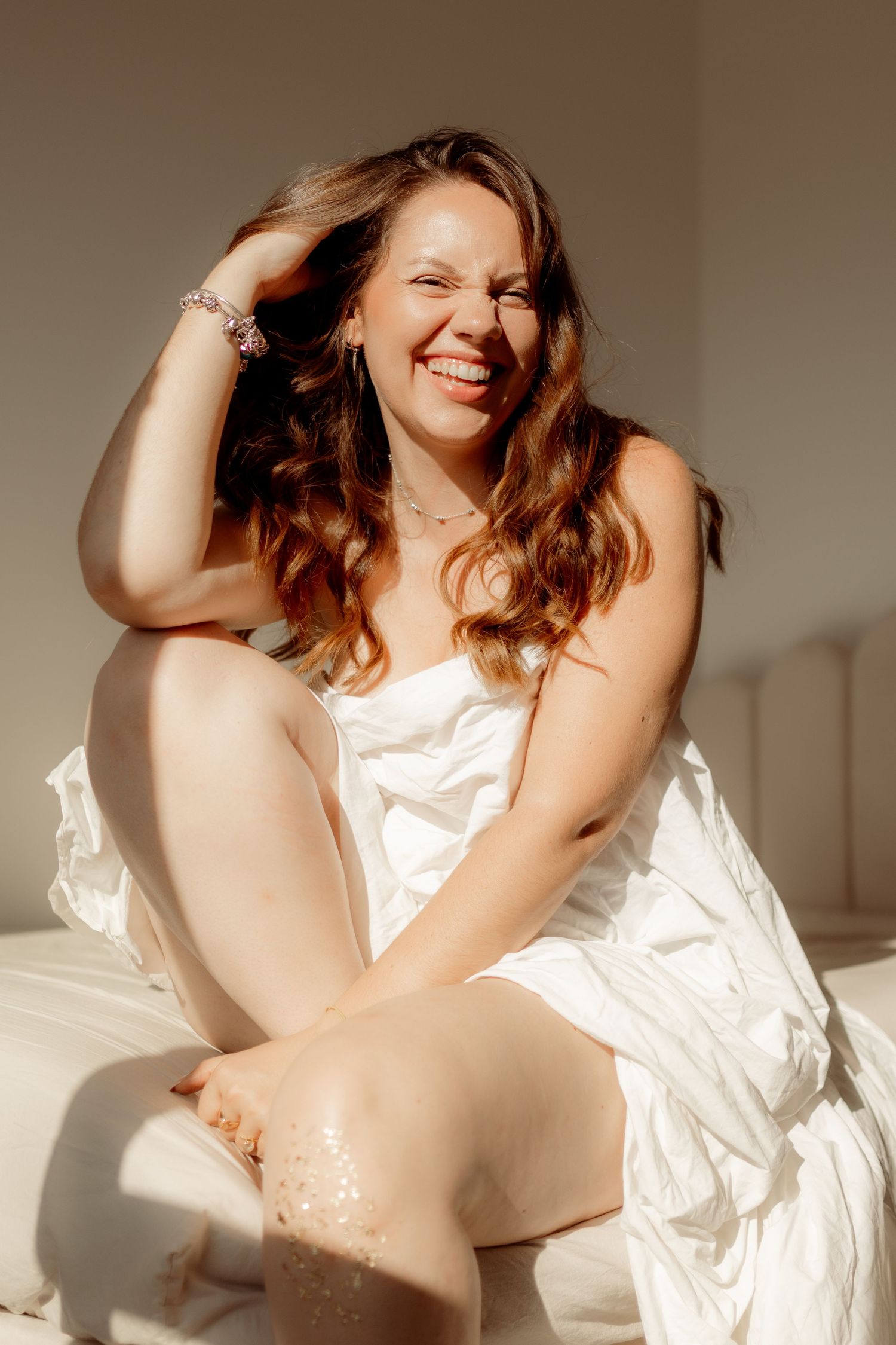 A person in white fabric lounges in soft sunlight creating a dreamy boudoir photoshoot series.