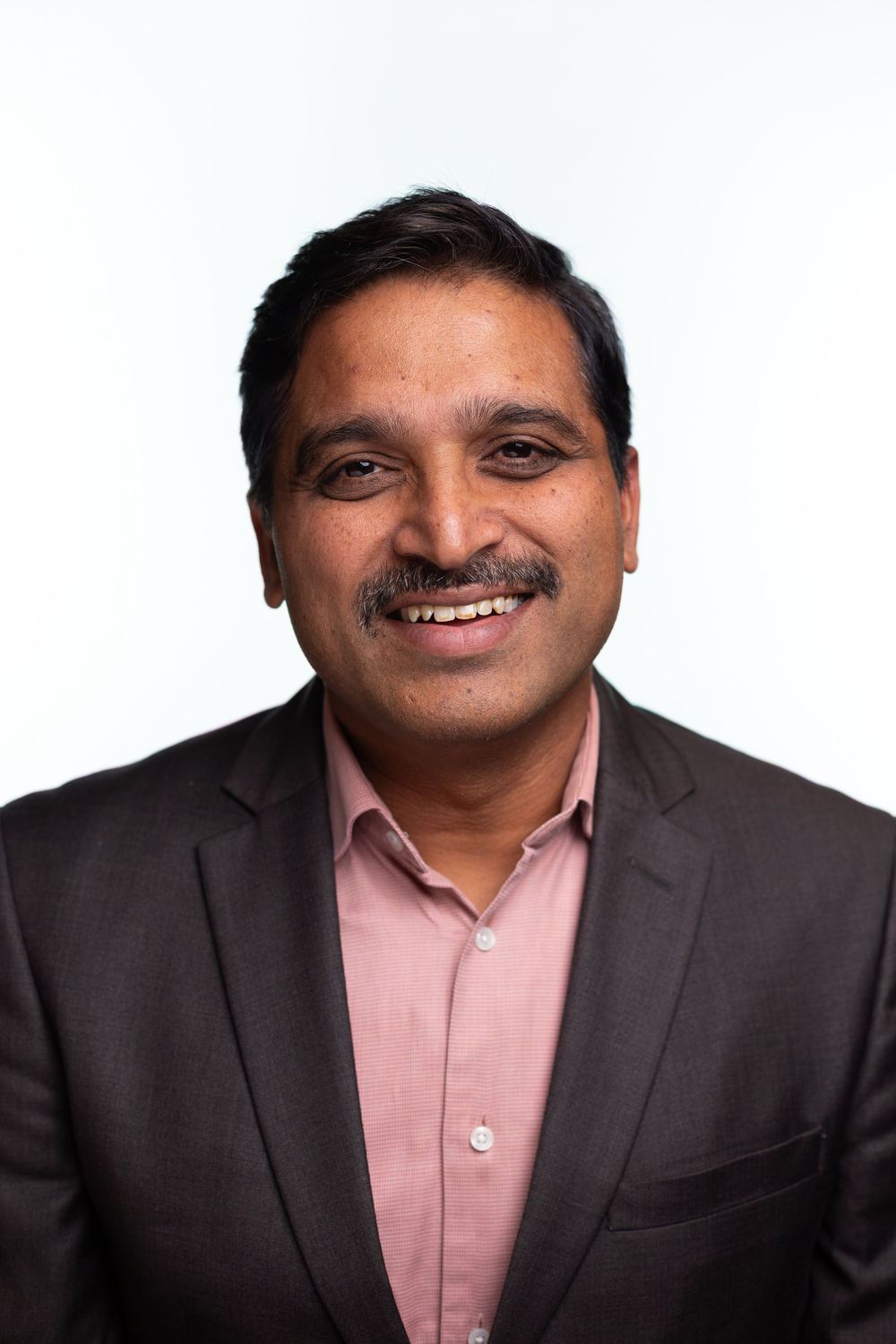 Professional headshots showing a person in a dark suit and pink shirt with a warm smile against white background.