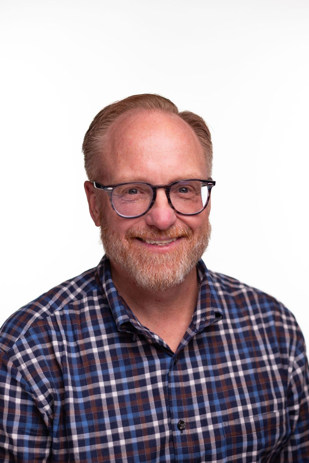 A person wearing glasses and a blue plaid shirt smiles warmly at the camera in a series of four similar headshots.