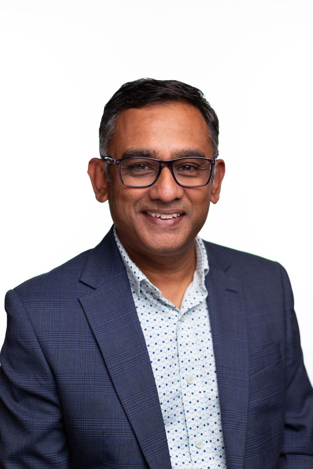 Professional headshot of someone in a navy suit jacket and polka dot dress shirt against a light background.