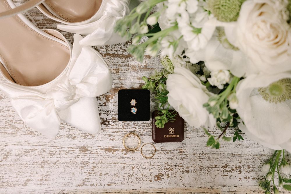 Coffee cups and white roses arranged on a rustic white wooden surface with scattered greenery and decor elements.