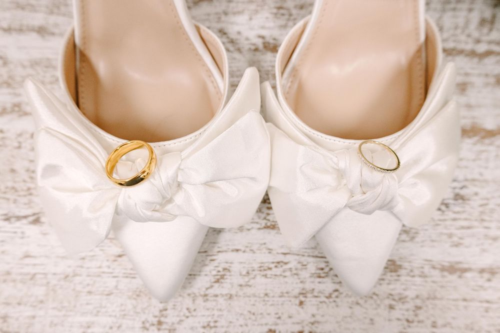 Elegant white bridal shoes with gold accents displayed on a rustic whitewashed wooden surface.