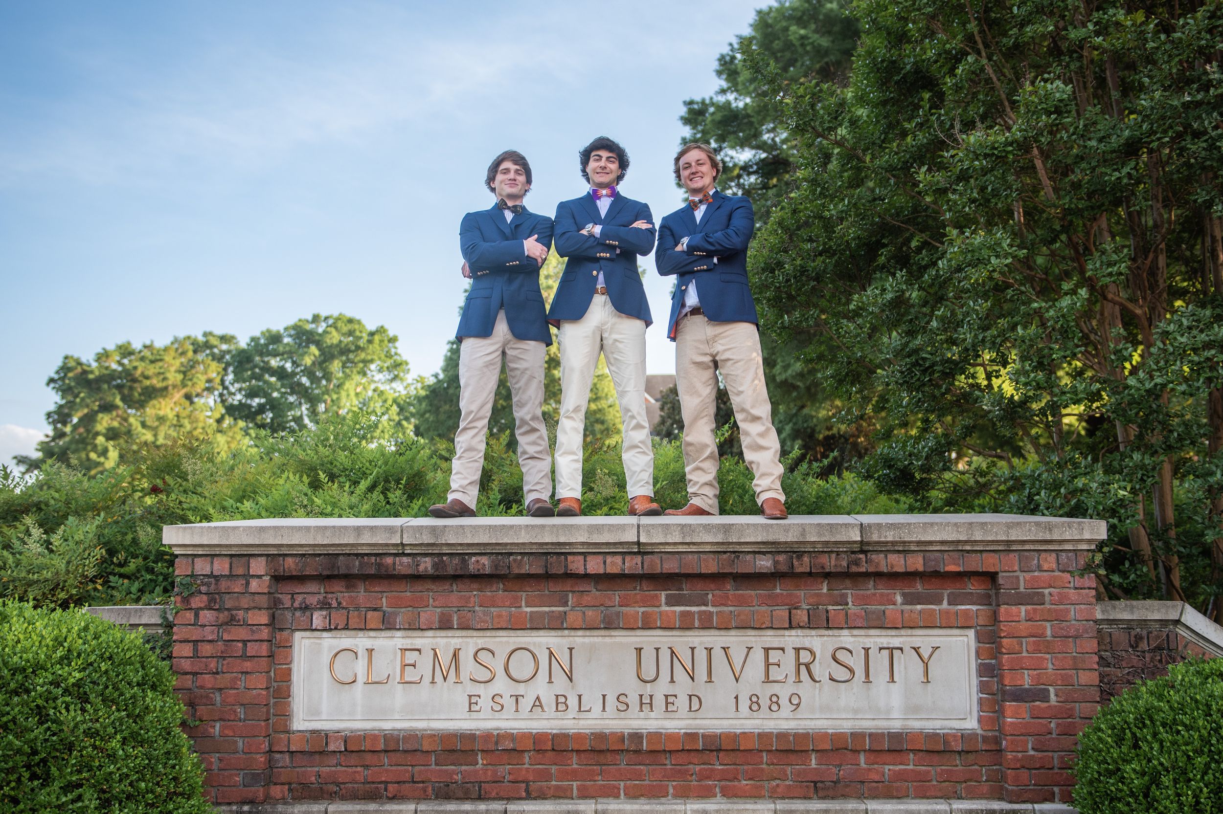 Students stand atop a brick entrance sign at Clemson University's historic gateway established in 1889.