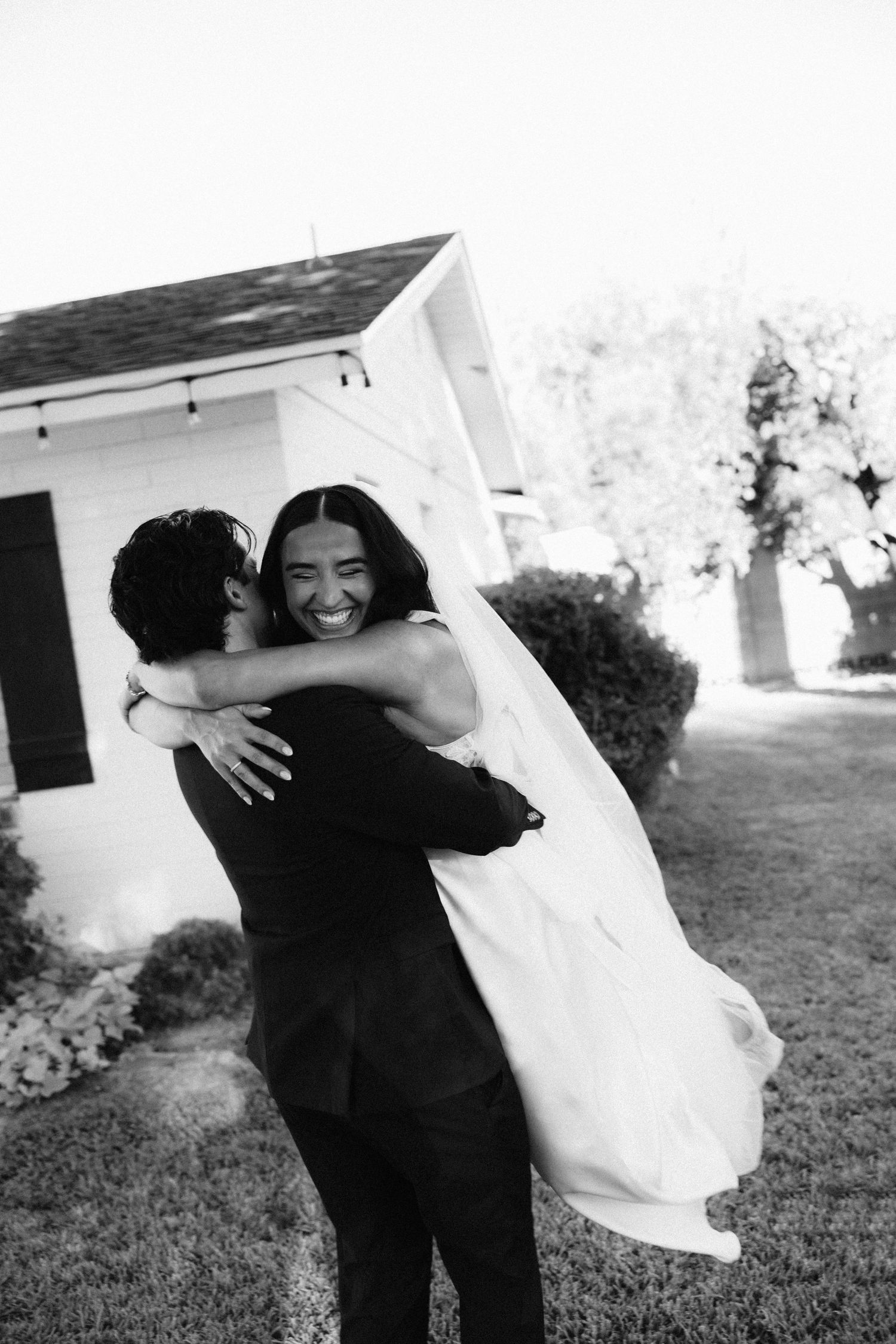 A series of four black and white wedding photos showing joyful embraces between people in formal attire outdoors.