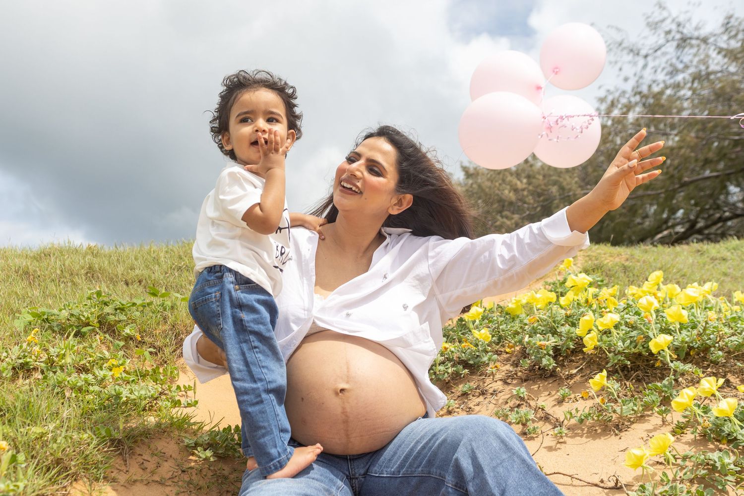 A joyful moment shared between parent and child in a flower-filled beach side with pink balloons floating in the background.