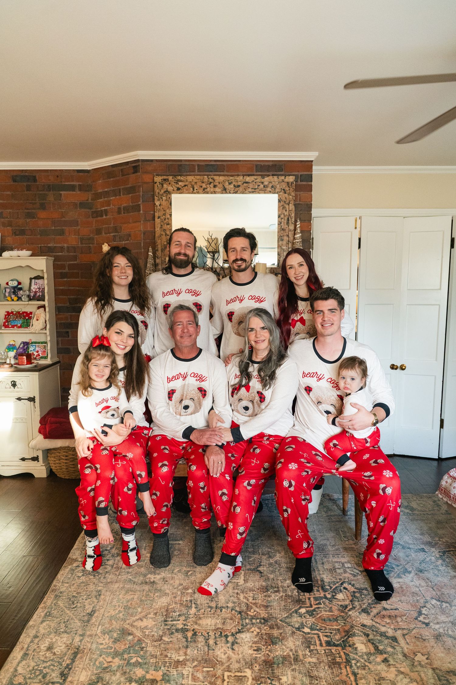 Family in bright red Christmas PJs smiling in front of the fireplace, photographed by a Fort Worth TX family photographer.