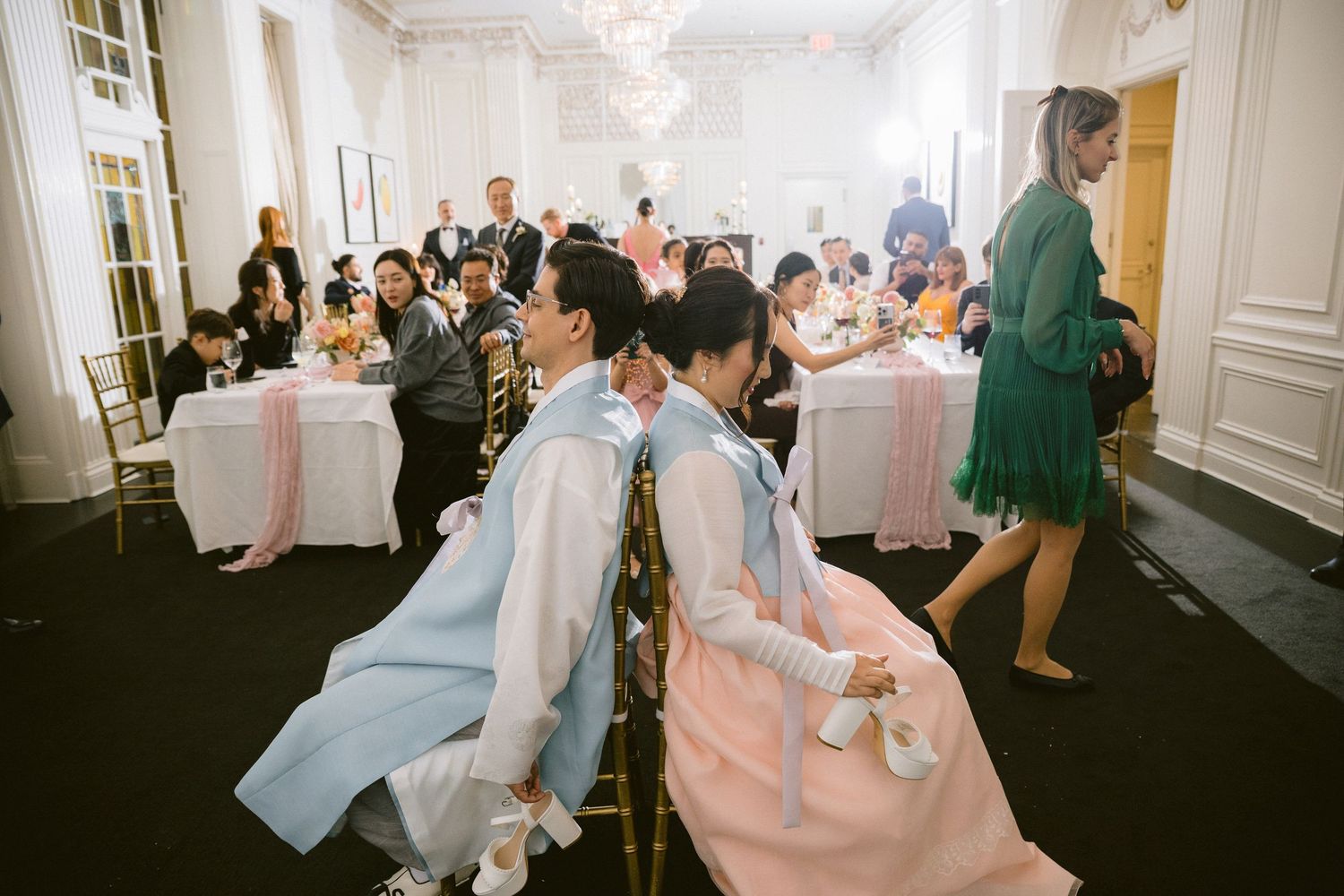 Guests dance and celebrate during an elegant wedding reception in a bright white ballroom with ornate moldings.