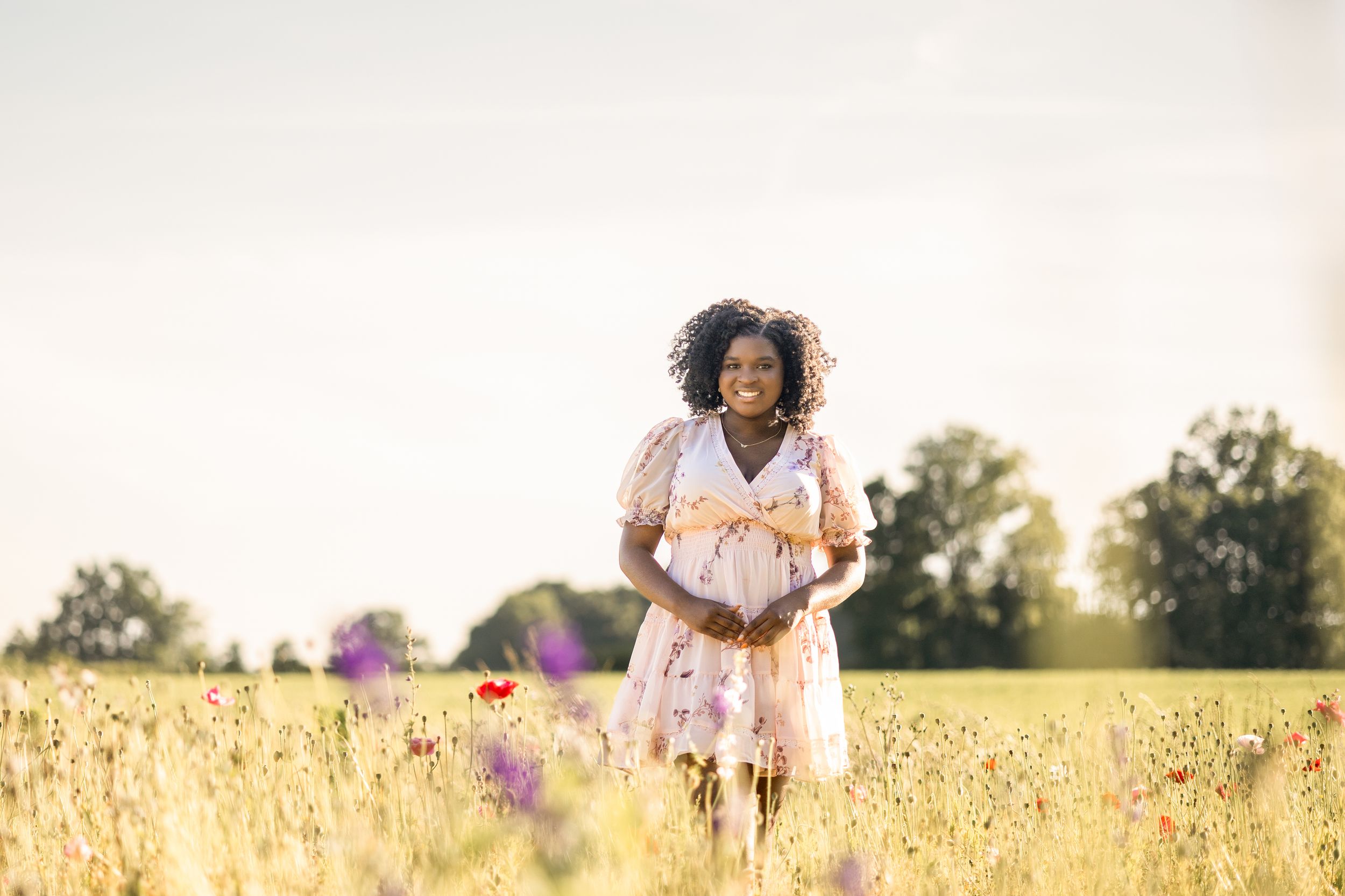 Person dances through a golden field at sunset wearing a flowing white dress among summer flowers.